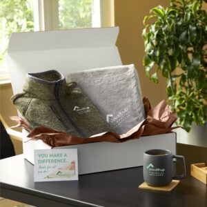 An open box neatly packed with a custom-branded half-zip sweater, coffee mug, and throw blanket, ready to be shipped to customers with a logo of their choice.